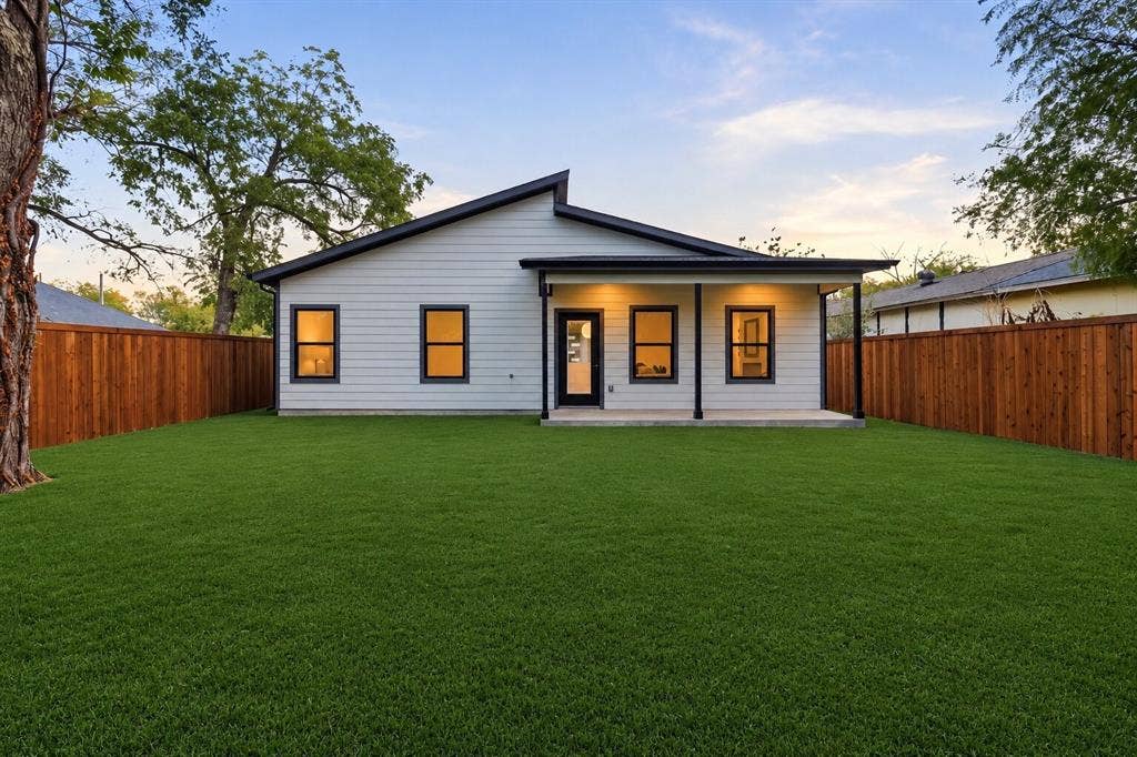 Modern single-story exterior featuring light-toned horizontal siding, an asymmetrical roofline, a covered rear porch, and a private fenced yard