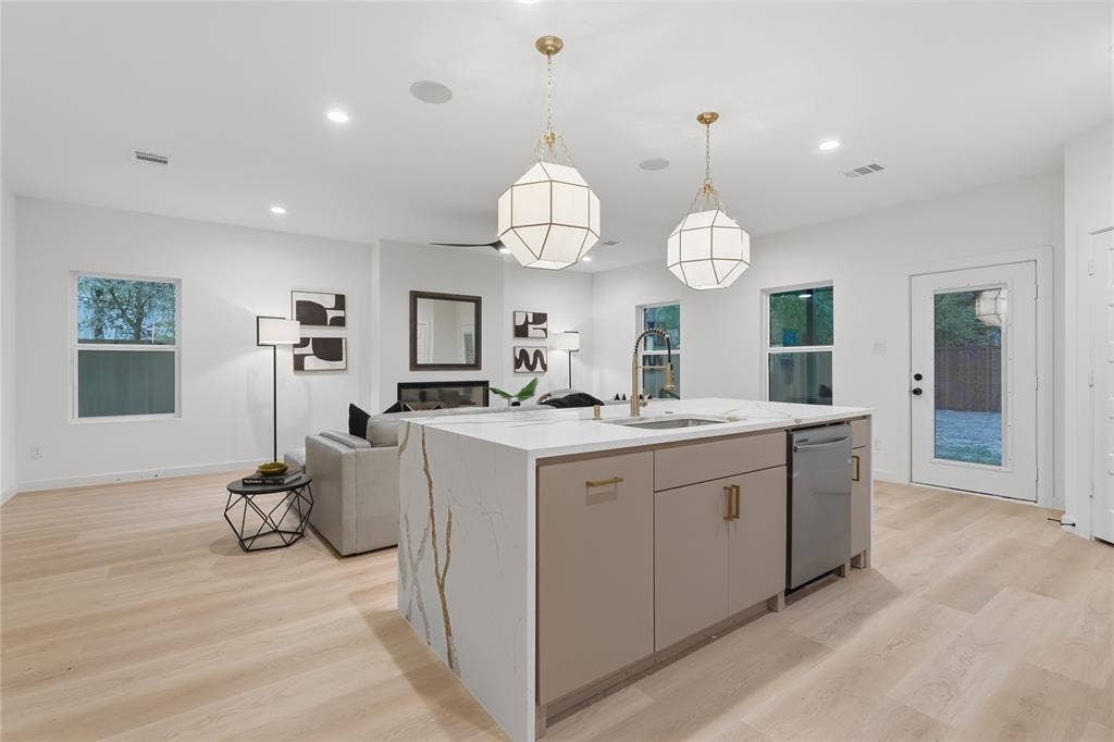 Kitchen island with stone-finish waterfall countertop, wood-finish flooring, dual geometric pendant lighting, built-in fireplace, and recessed ceiling lighting