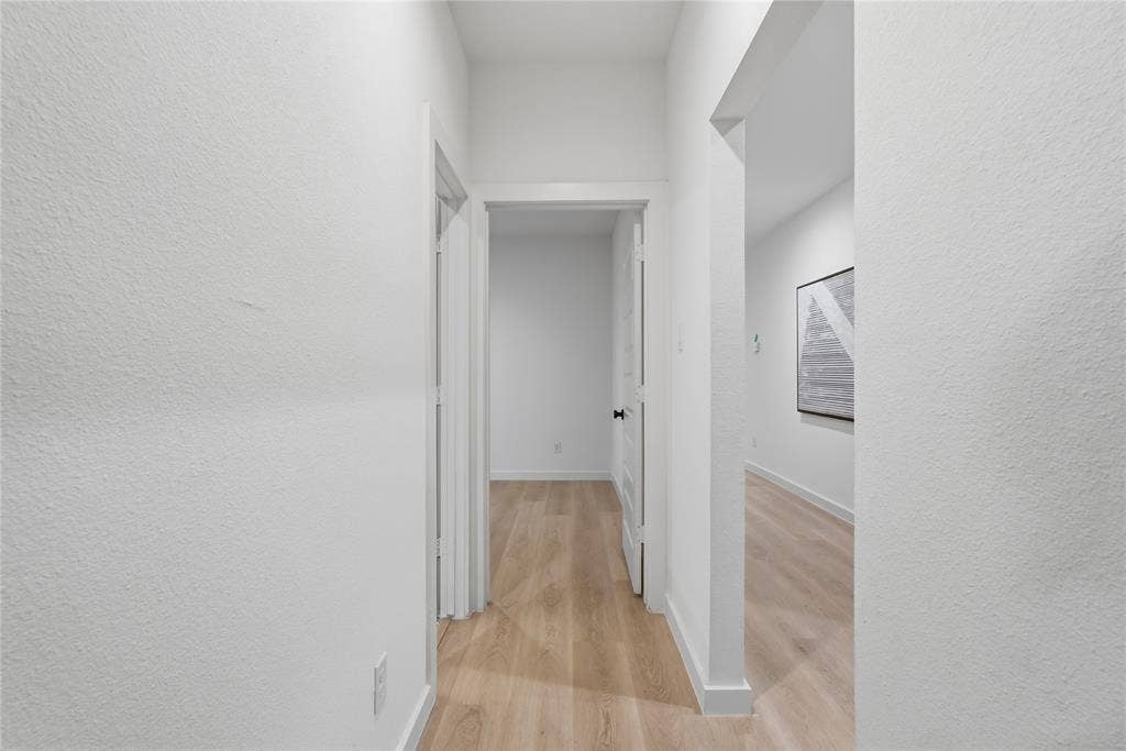 Interior hallway featuring white wall finishes, wood-finish flooring, and crisp door casing
