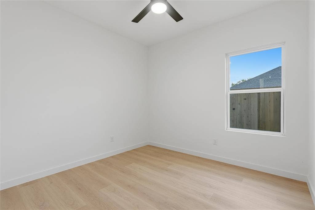 Neutral interior space featuring wood-finish flooring, a single-pane window, and a matte black ceiling fan with an integrated light fixture