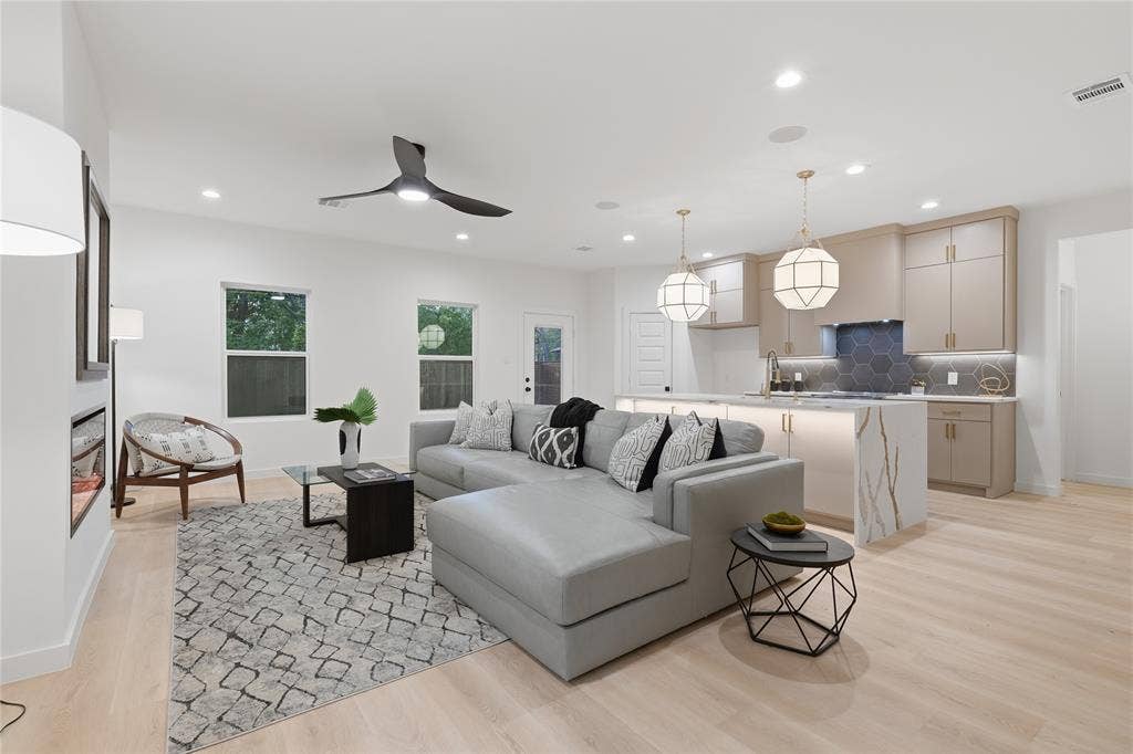 Open-concept interior featuring light wood-finish flooring, recessed lighting, a modern kitchen with quartz waterfall-edge island, hexagonal tile backsplash, and a wall-mounted electric fireplace