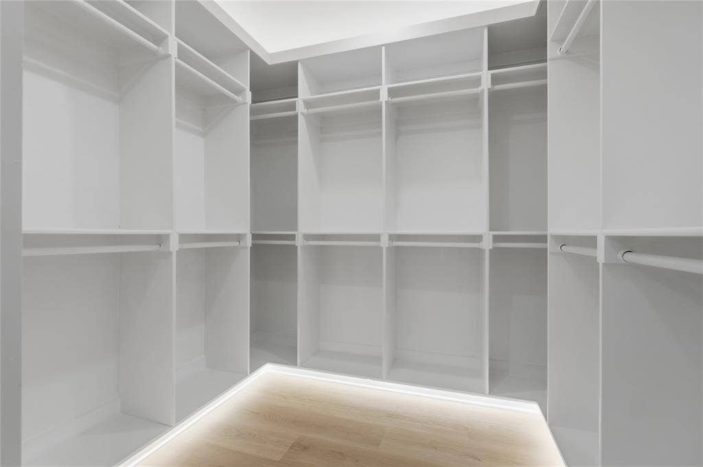 Custom walk-in closet featuring white built-in shelving, multiple hanging rods, and integrated floor-level LED accent lighting over wood-finish flooring