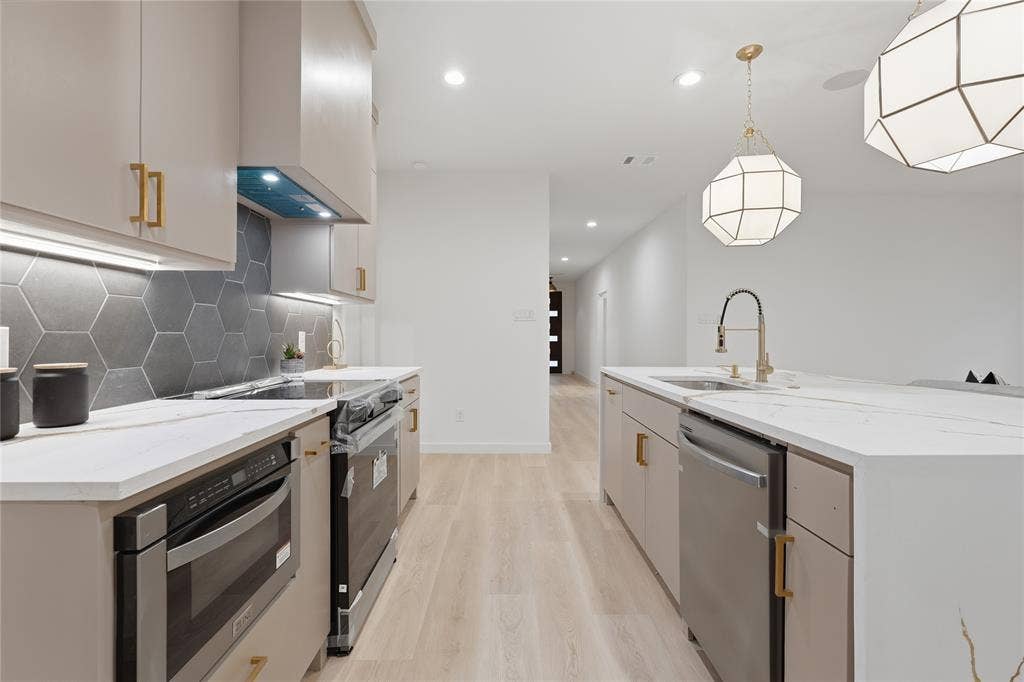 Kitchen featuring stone countertops, hexagonal tile backsplash, stainless steel appliances, wood-finish flooring, and geometric pendant lighting