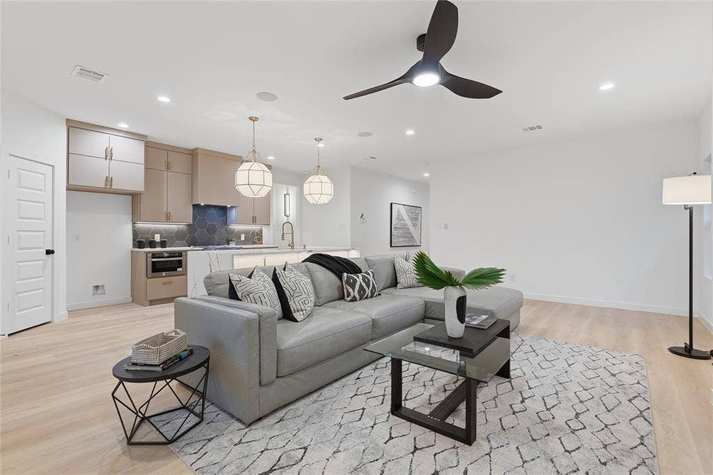 Open-concept space featuring wood-finish flooring, two decorative pendant lights, recessed ceiling lighting, a contemporary three-blade ceiling fan, and kitchen cabinetry with a geometric tile backsplash