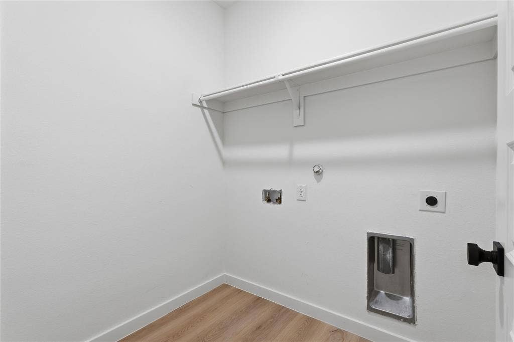 Utility area featuring wood-finish flooring, white walls, built-in overhead shelving, and dedicated water and electrical hookups