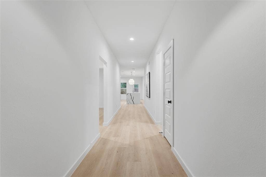 Hallway featuring light-toned wood-finish flooring, recessed lighting, and five-panel interior doors with matte black hardware
