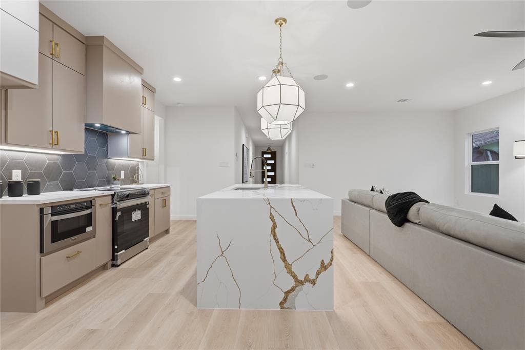 Kitchen featuring custom cabinetry, hexagon-patterned backsplash, quartz-topped island with integrated sink, wood-finish flooring, and geometric pendant lighting