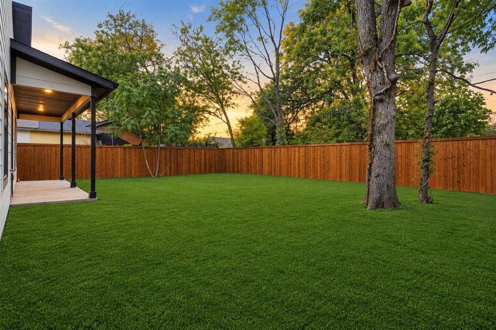 Backyard featuring a covered patio, synthetic turf lawn, full-height wood fencing, and mature trees