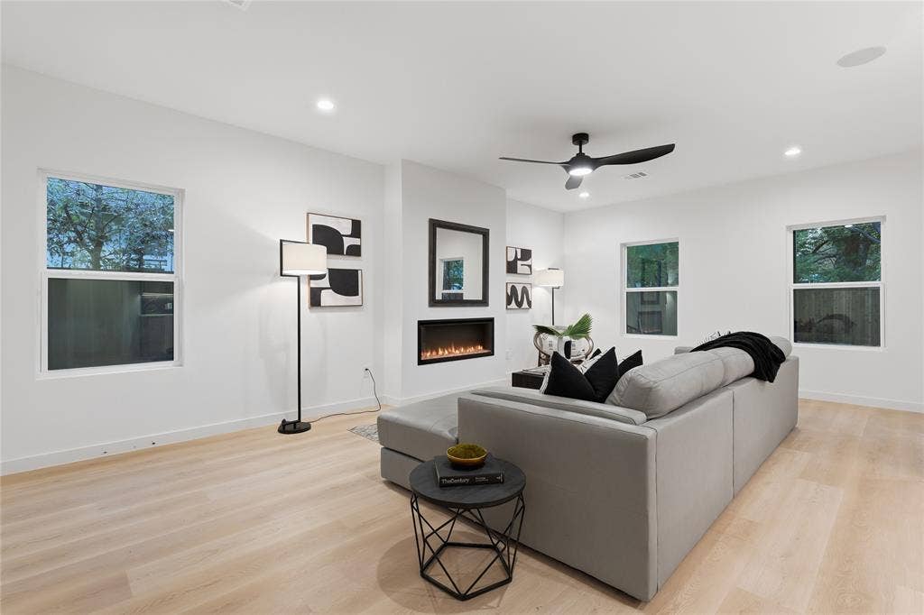 Living space featuring wood-finish flooring, recessed lighting, a ceiling fan with integrated lighting, and a linear built-in fireplace