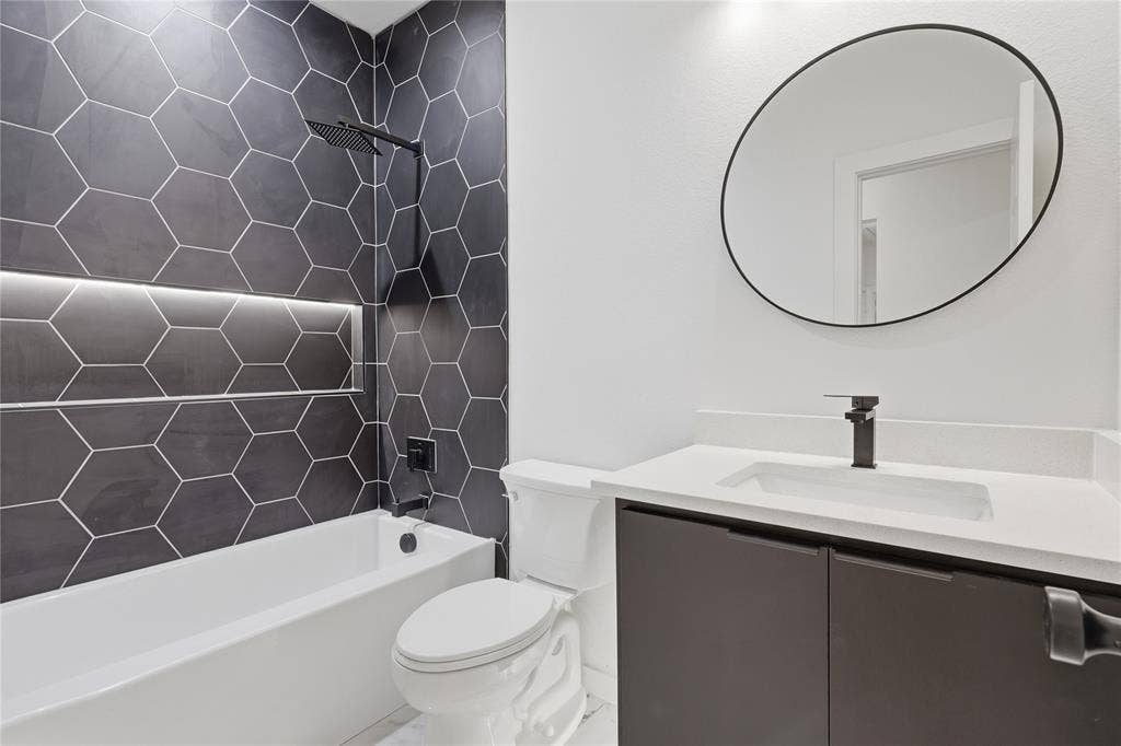 Bathroom featuring a charcoal hexagon tile surround with integrated recessed shelving, a wall-mounted matte black rainfall showerhead, a floating vanity with a stone-composite countertop, and an oval mirror