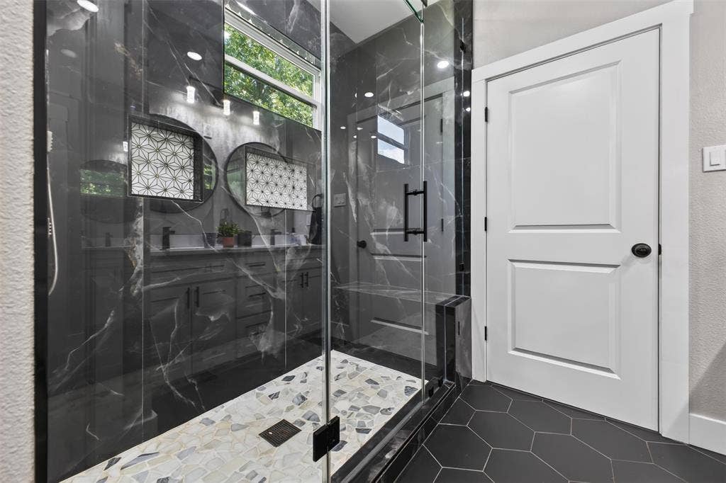 9116 Beckleycrest Avenue, Dallas, TX 75232 Primary bathroom offers an oversized walk-in shower with striking floor to ceiling marbled tile, frameless glass enclosure, built in shower bench and tiled flooring.