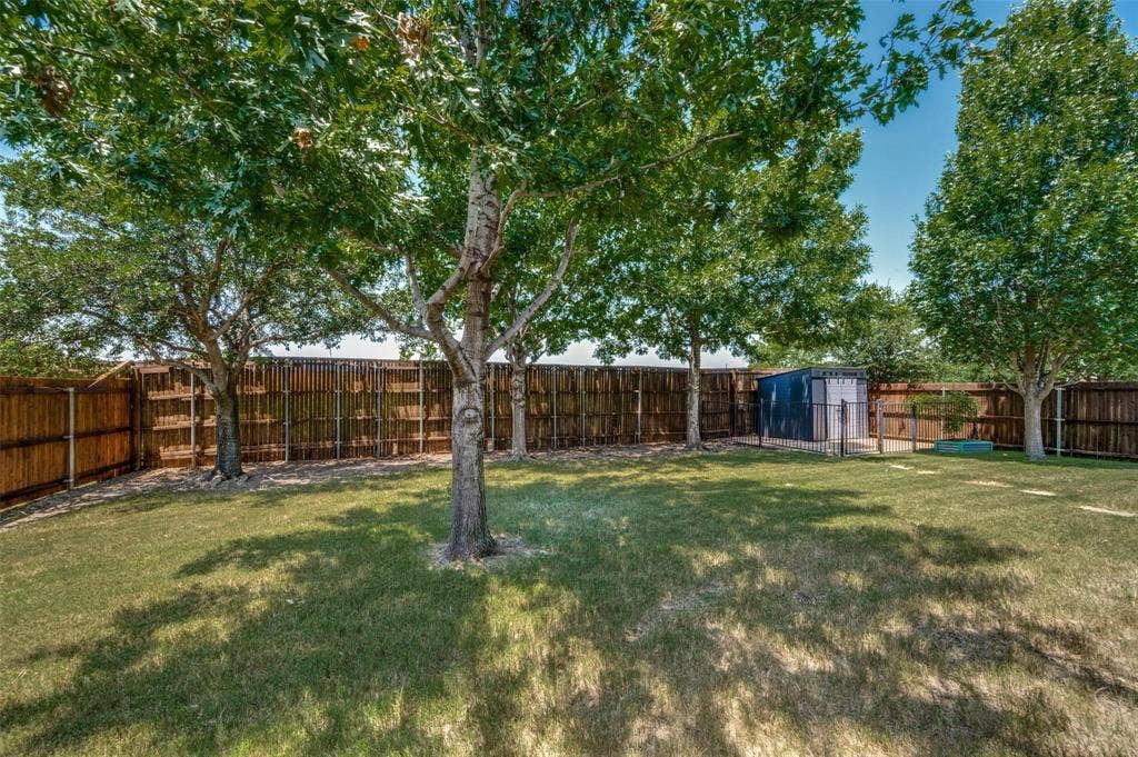1441 Kirkwood Lane, Prosper, TX 75078 Private backyard featuring a sprawling lawn, mature trees, wood privacy fencing, and a detached storage structure