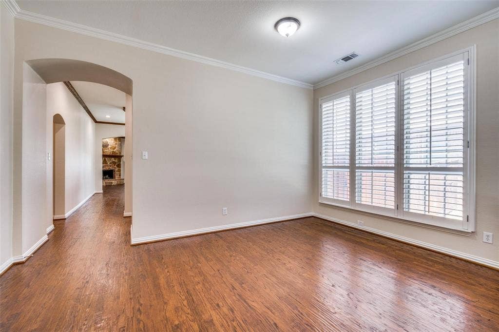 1441 Kirkwood Lane, Prosper, TX 75078 Room featuring wood-finish flooring, crown molding, multi-panel window with plantation shutters, and an arched entryway