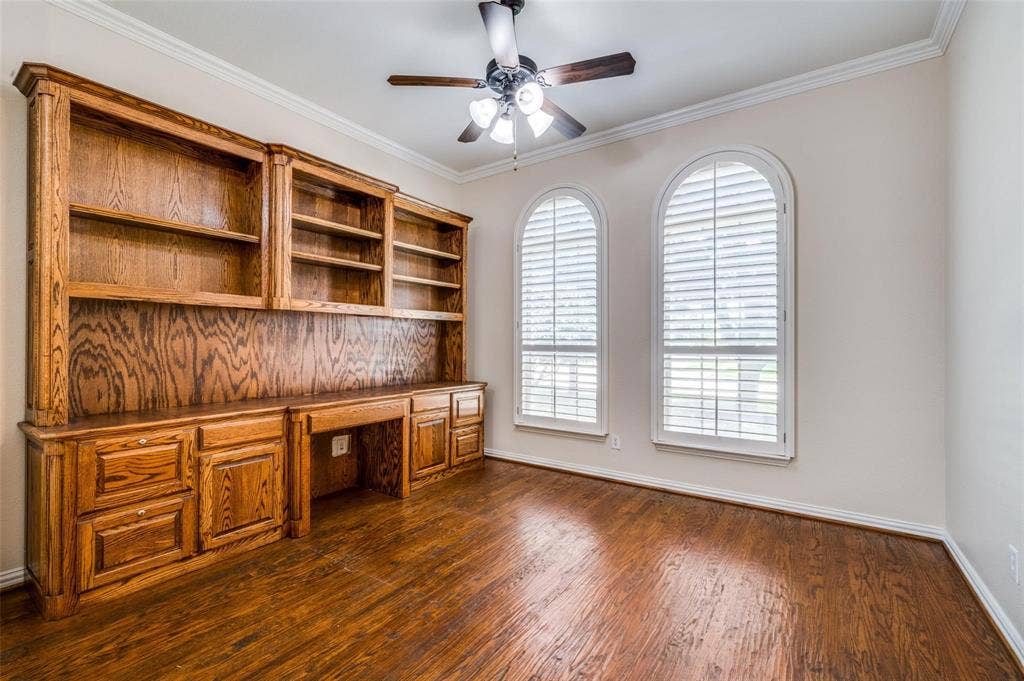 1441 Kirkwood Lane, Prosper, TX 75078 Custom built-in oak cabinetry with integrated shelving and desk workspace, arched windows with plantation shutters, wood-finish flooring, and crown molding