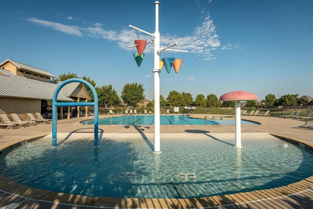 1441 Kirkwood Lane, Prosper, TX 75078 Zero-depth entry splash pad featuring a water feature with dumping buckets and a mushroom-shaped water fountain, accompanied by a full-size lap pool and concrete pool deck