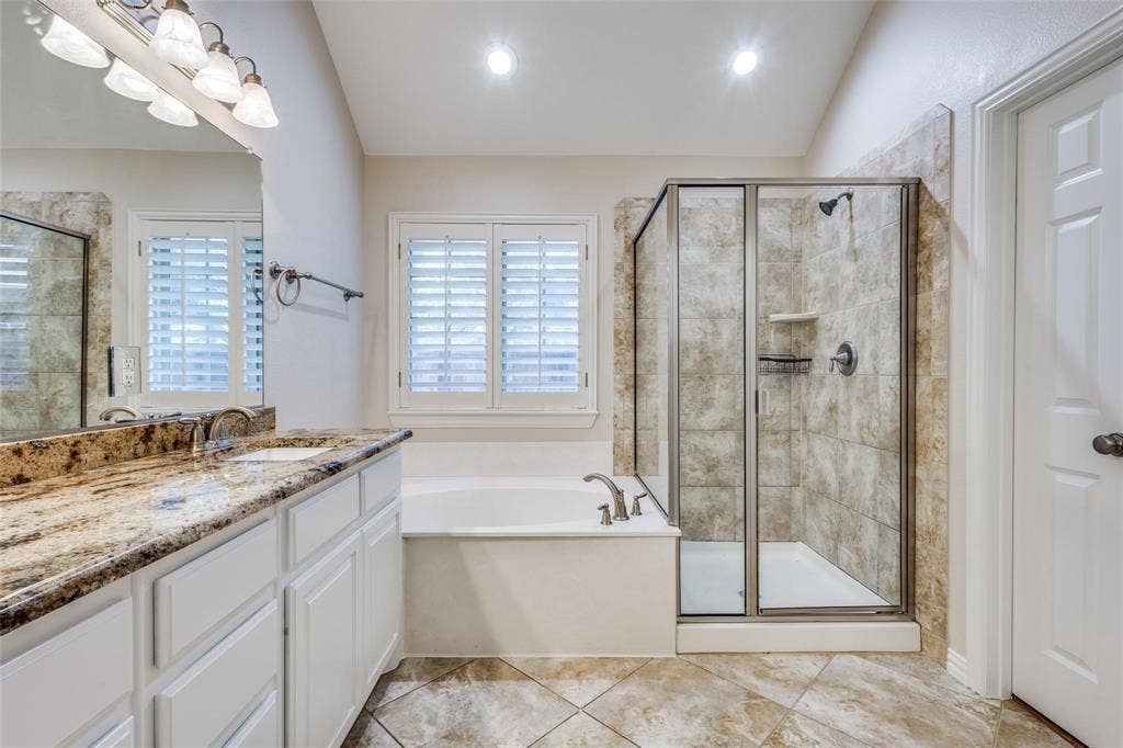 1441 Kirkwood Lane, Prosper, TX 75078 Bathroom featuring a white cabinetry vanity with a stone countertop, a deep soaking tub, and a glass-enclosed shower with tiled walls and flooring