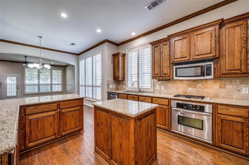 1441 Kirkwood Lane, Prosper, TX 75078 Kitchen featuring wood cabinetry, stone countertops, stainless steel appliances, wood-finish flooring, and plantation shutters