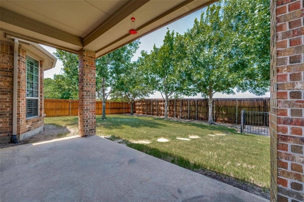 1441 Kirkwood Lane, Prosper, TX 75078 Covered concrete patio featuring brick structural pillars, enclosed by a wood privacy fence and mature trees