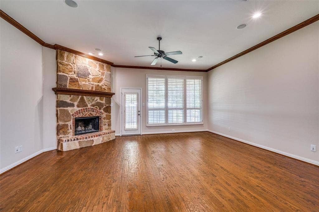 1441 Kirkwood Lane, Prosper, TX 75078 Living area featuring wood-finish flooring, a floor-to-ceiling stone fireplace with a brick hearth, crown molding, a ceiling fan, and large windows with plantation shutters