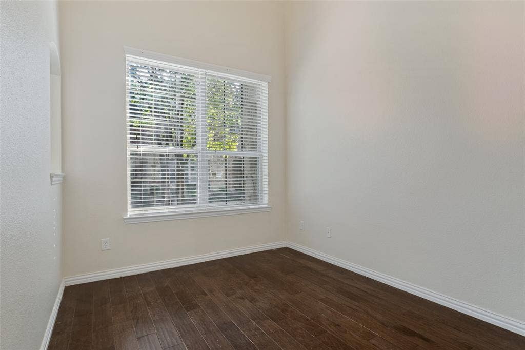 High-ceiling room featuring dark wood-finish flooring, neutral wall paint, and a large window with white horizontal blinds