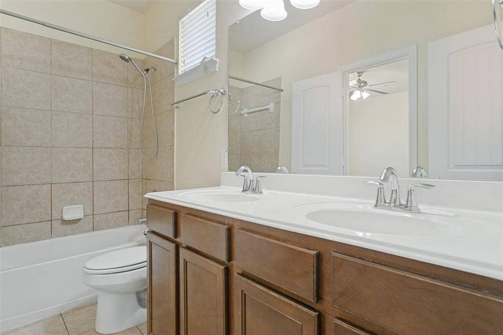 Dual-sink vanity with wood-finish cabinetry, white countertop, oversized wall mirror, and tile-surround shower-tub combination