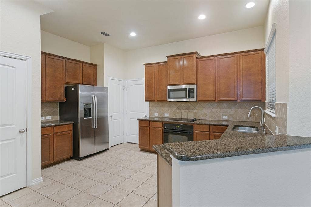 Kitchen featuring wood cabinetry, stone-surface countertops, tile backsplash, stainless steel refrigerator, and recessed lighting