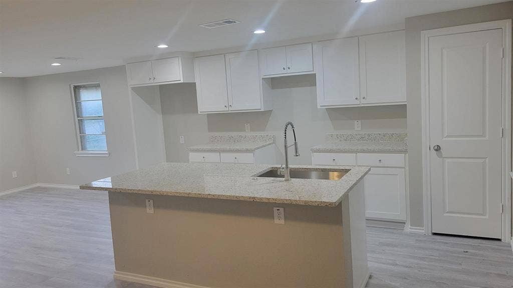 707 Korgan Street, Dallas, TX 75216 Kitchen featuring white shaker-style cabinetry, stone-finish countertops, a center island with an undermount stainless steel sink, gooseneck faucet, and wood-finish flooring
