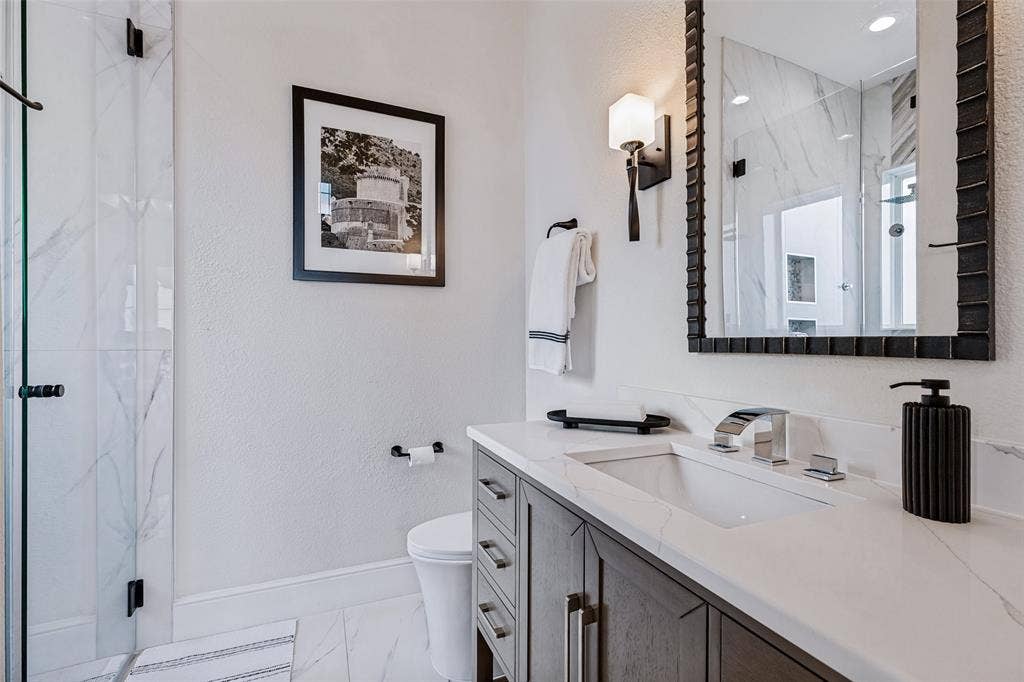 4604 Devon Drive, Parker, TX 75002 Bathroom featuring a vanity with quartz countertop, dark wood-finish cabinetry, a glass-enclosed shower with stone-patterned tile, and wall-mounted light fixtures