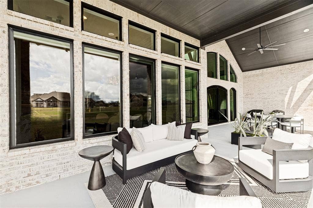 4604 Devon Drive, Parker, TX 75002 Covered outdoor living area featuring light-colored brick masonry, extensive floor-to-ceiling windows with transom accents, and a dark-finished tongue-and-groove ceiling with a built-in ceiling fan