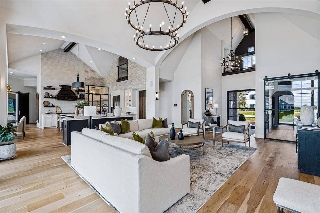 4604 Devon Drive, Parker, TX 75002 Vaulted ceilings with exposed structural beams, wide-plank wood-finish flooring, floor-to-ceiling stone-clad wall, oversized tiered metal chandeliers, and black-framed sliding glass partition