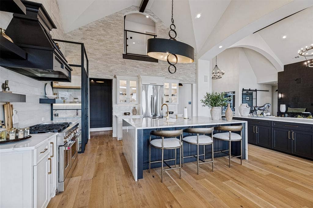 4604 Devon Drive, Parker, TX 75002 Vaulted ceilings, floor-to-ceiling stone accent wall, oversized central island with waterfall-edge countertop, professional-grade range with custom hood, and wood-finish flooring