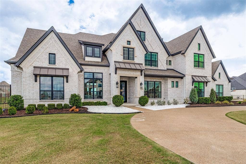 4604 Devon Drive, Parker, TX 75002 Multi-gabled exterior featuring white brick masonry, dark metal roof accents, multi-pane windows with dark frames, stone-surround entryway, and a concrete aggregate driveway