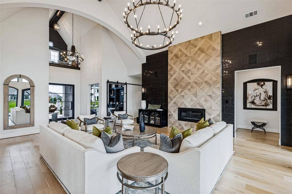 4604 Devon Drive, Parker, TX 75002 Vaulted ceiling with arched structural detailing, floor-to-ceiling fireplace featuring geometric patterned tile inlay, black tile accent wall, wide-plank wood-finish flooring, and large double-tier circular chandelier