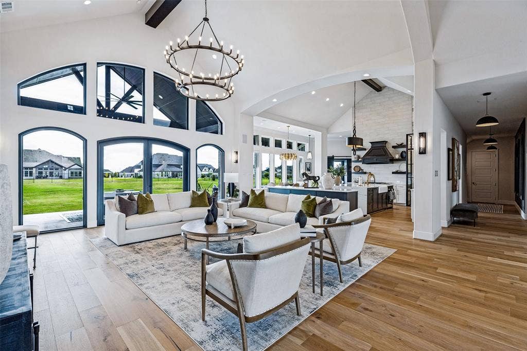 4604 Devon Drive, Parker, TX 75002 Vaulted ceilings with exposed timber beams, expansive arched windows, wide-plank wood-finish flooring, custom iron chandelier, and a floor-to-ceiling masonry fireplace facade
