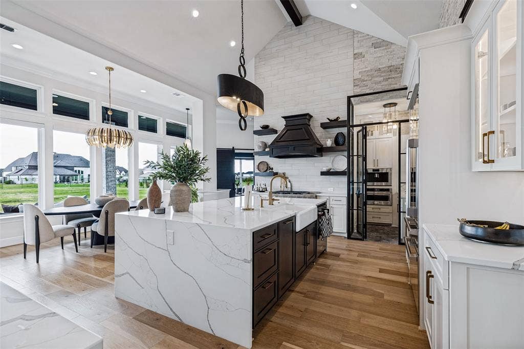 4604 Devon Drive, Parker, TX 75002 Kitchen featuring a vaulted ceiling with a stacked-stone accent wall, expansive quartz waterfall island, custom matte black cabinetry, and wood-finish flooring