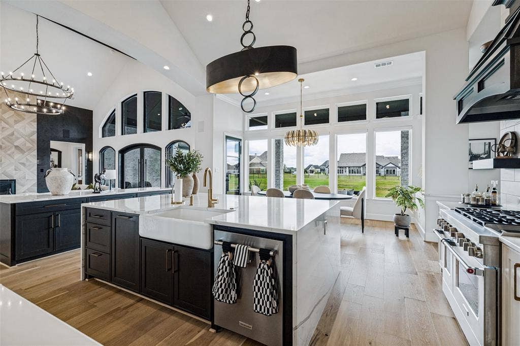 4604 Devon Drive, Parker, TX 75002 Kitchen featuring a large central island with quartz countertops and a farmhouse-style apron sink, custom dark cabinetry, high-end stainless steel range, and wood-finish flooring under vaulted ceilings