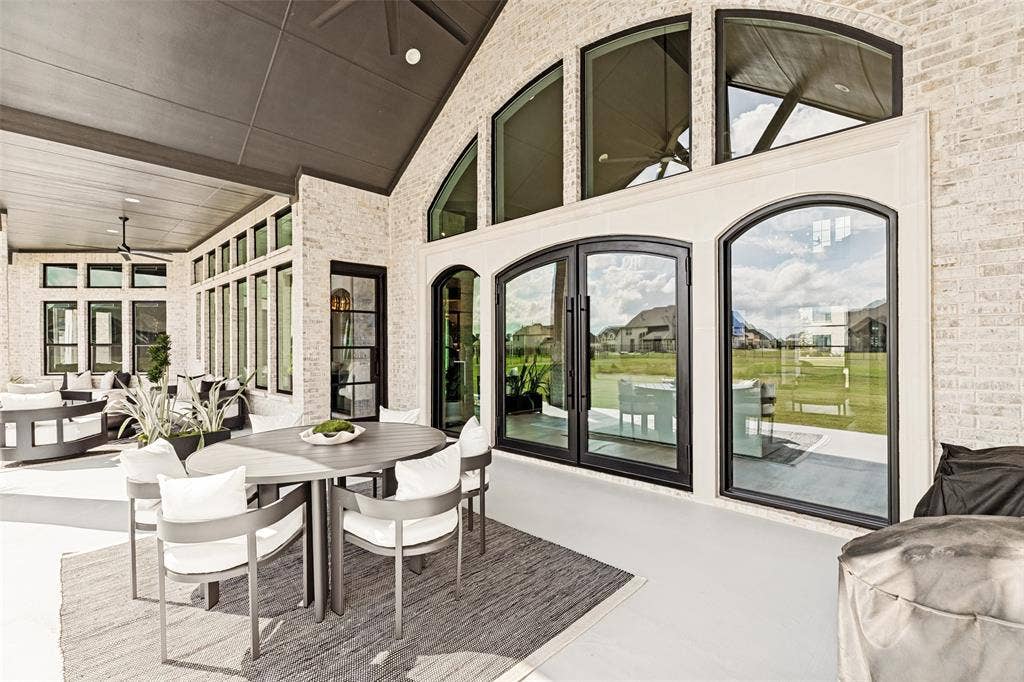 4604 Devon Drive, Parker, TX 75002 Covered patio featuring white brick exterior walls, dark-framed arched glass double doors, expansive fixed-pane arched transom windows, and a vaulted ceiling with integrated recessed lighting