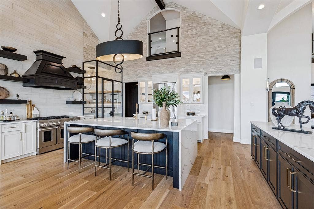 4604 Devon Drive, Parker, TX 75002 Vaulted ceiling featuring a floor-to-ceiling stone accent wall, center island with stone countertop, professional-grade range with custom hood, glass-enclosed pantry, and wood-finish flooring