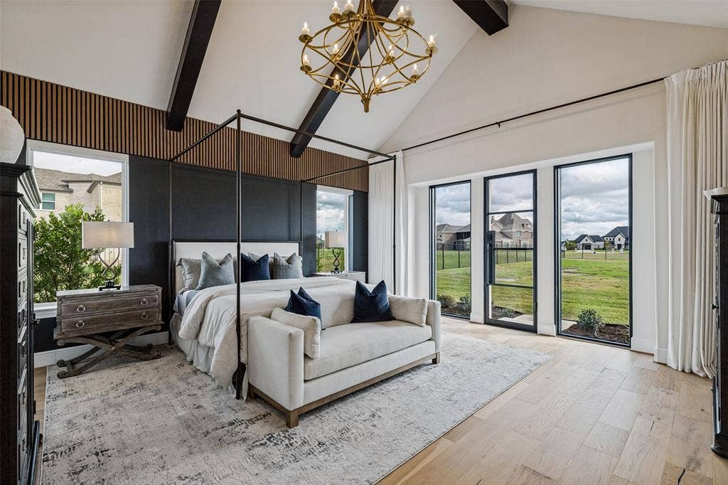 4604 Devon Drive, Parker, TX 75002 Vaulted ceiling with exposed dark wood beams, vertical slat wood accent wall, floor-to-ceiling multi-panel windows with black frames, brass-finish tiered chandelier, and light wood-finish flooring