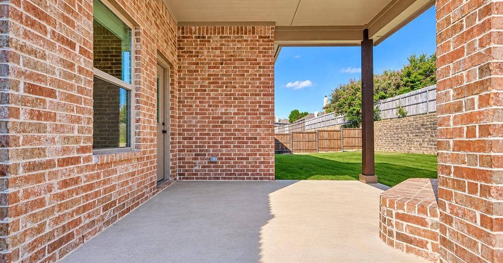 632 Grisham Drive, Fate, TX 75087 Covered concrete patio featuring brick exterior walls, a built-in brick sitting wall, and supporting structural columns