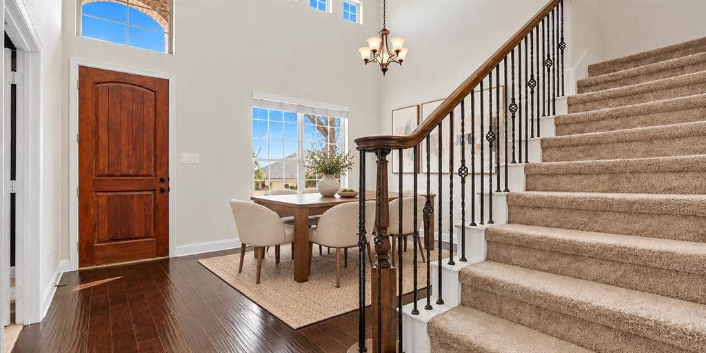 632 Grisham Drive, Fate, TX 75087 Double-height entryway featuring dark wood-finish flooring, a multi-pane arched transom window, a wood-finish entry door, and a staircase with an ornamental metal balustrade and wood handrail