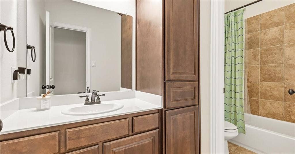 632 Grisham Drive, Fate, TX 75087 Bathroom vanity featuring stained wood cabinetry, a white countertop with an integrated oval sink, matte black hardware, and an expansive wall-mounted mirror