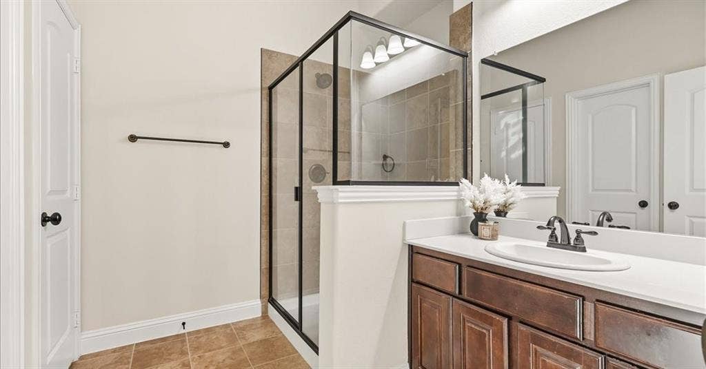 632 Grisham Drive, Fate, TX 75087 Bathroom featuring a walk-in shower with black-finish framing, neutral tile surround, vanity with cabinetry, solid-surface countertop, and an integrated oval sink