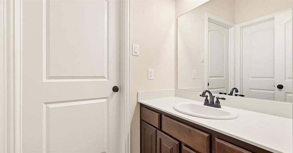 632 Grisham Drive, Fate, TX 75087 Bathroom vanity featuring dark-stained wood cabinetry, a solid-surface countertop with an integrated oval sink, a matte-finish dark faucet, and a large wall-mounted mirror