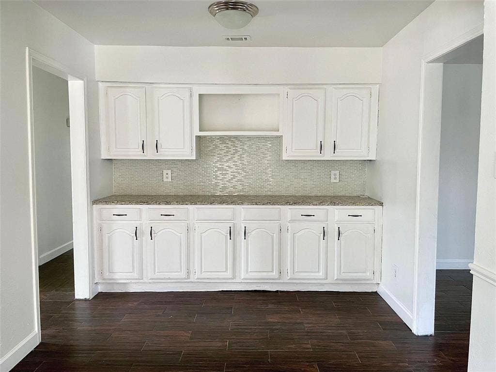 Dining area featuring white cabinetry, stone-finish countertops, decorative mosaic tile backsplash, and dark wood-finish flooring