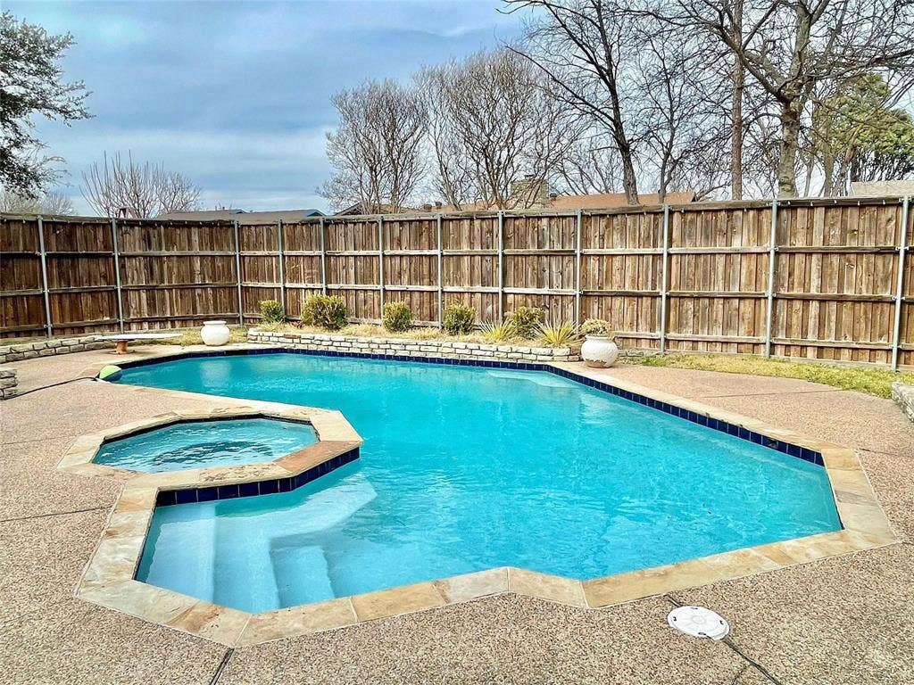 In-ground swimming pool with an attached spa, expansive exposed aggregate decking, stone-accented perimeter border, and a wood privacy fence