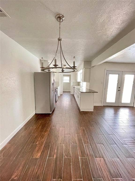 Wood-finish flooring, white cabinetry, neutral stone-finish countertops, stainless steel refrigerator, and a circular brushed-metal chandelier