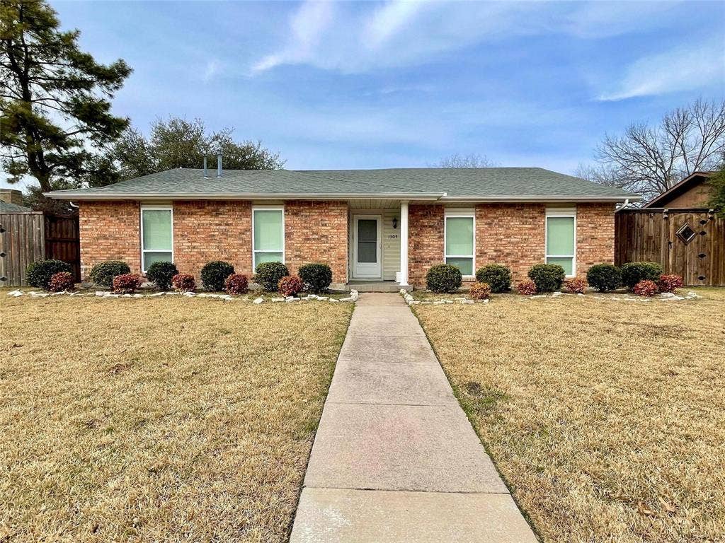 Single-story brick exterior featuring a multi-gabled roofline, concrete walkway, and manicured ornamental shrubbery