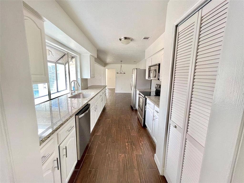 Kitchen featuring white cabinetry, stone-finish countertops, stainless steel appliances, wood-finish flooring, and louvered-door pantry storage
