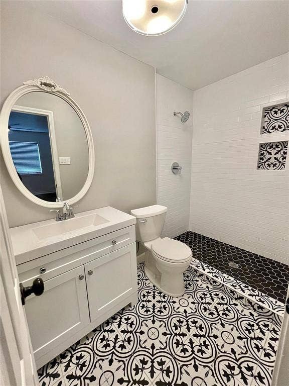 Primary Bathroom featuring a white vanity with a rectangular sink, patterned floor tile, a walk-in shower with horizontal wall tile, two built-in shower niches with decorative tile, and an oval wall mirror